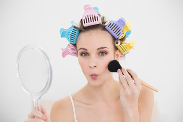 Funny natural brown haired woman in hair curlers applying powder on her face