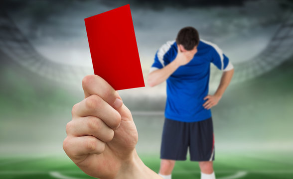 Composite image of hand holding up red card to player against football pitch in large stadium 