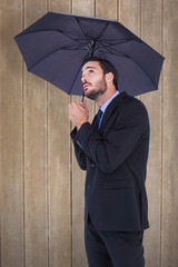 Businesswoman in suit holding umbrella while looking up against wooden surface with planks