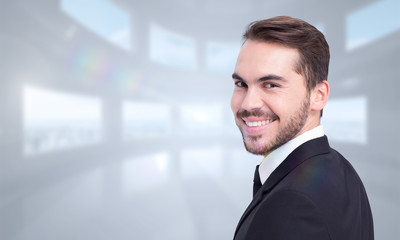 Naklejka na ściany i meble Elegant businessman in suit smiling at camera against bright white room with windows