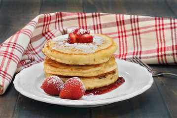 Pancakes, in a stack, with fresh strawberries and powdered sugar.