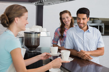Smiling waitress giving coffee to a couple at coffee shop