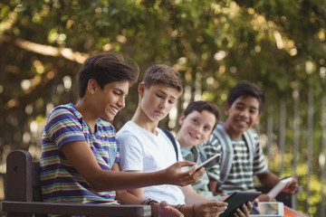 Obraz premium School kids using mobile phone and digital tablet on bench