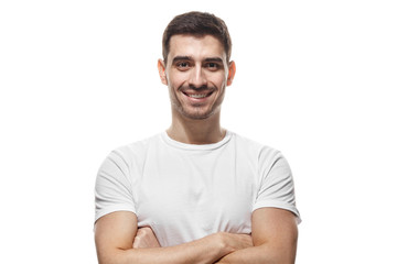 Fototapeta premium Closeup photo of young handsome European Caucasian male isolated on white background wearing white blank T-shirt, smiling, standing with arms crossed pressed to chest, looking strong and happy