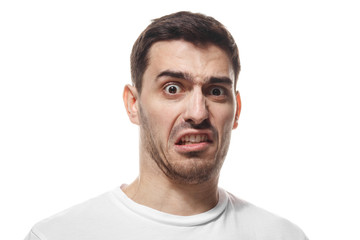 Closeup headshot of young Caucasian guy isolated on white background wearing white blank T-shirt showing strong emotion of disgust as if having smelled something stinky or met something unpleasant - obrazy, fototapety, plakaty