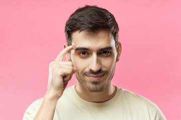 Closeup portrait of young European Caucasian man pictured isolated on pink background pressing finger to temple as if making viewer think more about offer or analyze information better for their good - obrazy, fototapety, plakaty