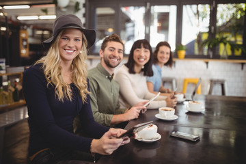 Smiling multi ethnic friends sitting with coffee cups and mobile phones at table