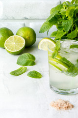 Mojito cocktail on white concrete table. Cold summer alcohol drink with ice, mint and lime. Vertical photo. 
