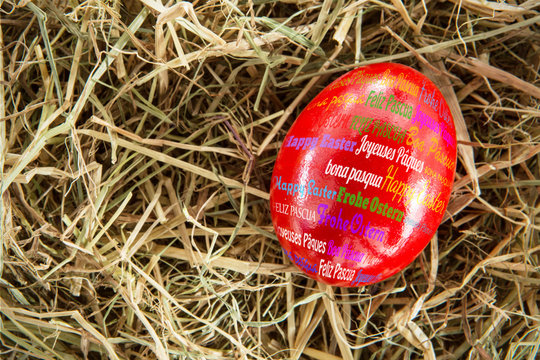 Happy easter in different languages against red egg on straw