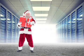 Santa carrying gifts against server hallway in desert setting