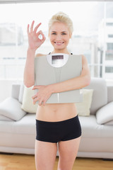 Woman carrying scale while gesturing okay sign