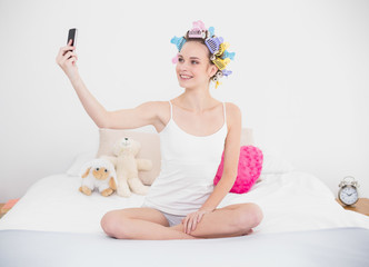 Obraz na płótnie Canvas Content natural brown haired woman in hair curlers taking a picture of herself with mobile phone