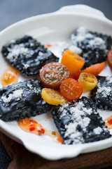 Black italian ravioli served with cherry tomatoes and topped with grated parmesan, closeup, vertical shot