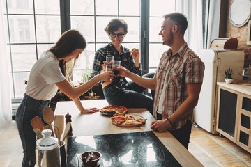 Friends clinking glasses with wine and eating pizza at home part