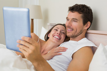 Happy couple using digital tablet in bed