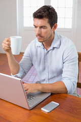 Man drinking coffee and using laptop at home