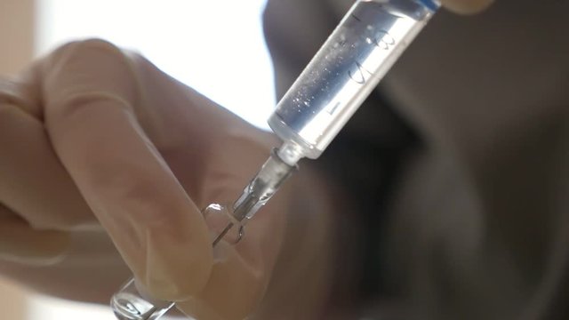 An impressive view of some hands keeping a syringe and an ampule with medicament. Gradually the liquid fills the suringe placed askew in a room