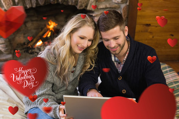 Couple using laptop in front of lit fireplace against happy valentines day