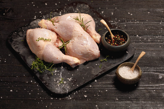 Raw chicken legs with solt andpepper in old clay dish on a black wooden rustic background. Copy space