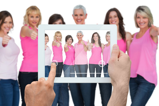 Composite image of hand holding tablet pc showing photograph of breast cancer activists