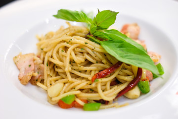 The spaghetti spicy bacon and ham with basil, tomato, black pepper, lettuce and paprika on white dish set on table for food background or texture - homemade food concept.