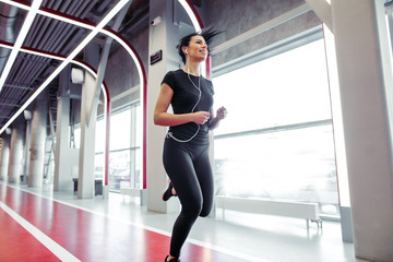Fit female athlete listening music and running on indoor track at gym