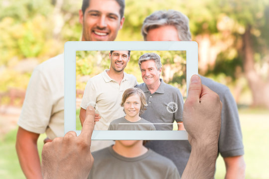 Hand holding tablet pc showing family looking at the camera in the park