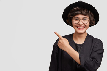 Adorable cute young female seller of clothes, being in good mood, advertises new outfit indoor,...