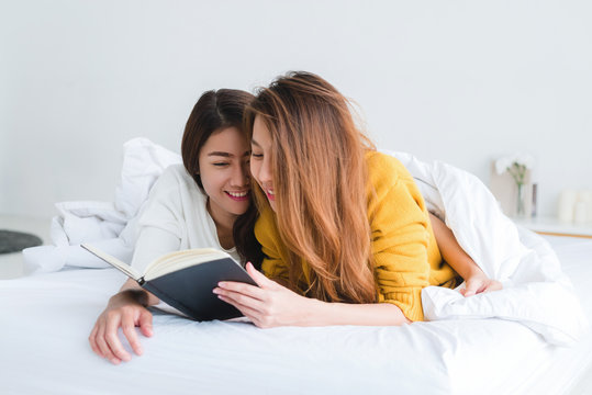Beautiful young asian women LGBT lesbian happy couple reading book lying together in bed under blanket at home. LGBT lesbian couple together indoors concept. Spending nice time at home.