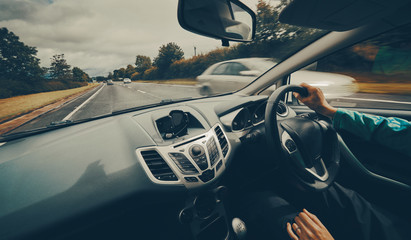 A female driver driving a car along a busy road on an English single carriageway on a cloudy overcaste day. Filter and styling applied. - obrazy, fototapety, plakaty