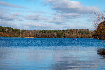 Boat floating on the blue water of the reservoir, sunny weather, blue sky in the clouds, in the distance you can see the forest, windy weather and water surface covered with ripples
