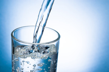 Pouring water into glass on blue background