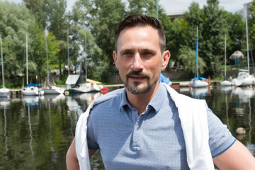 Portrait of handsome happy man near of river with boats. River cruise for successful men