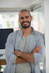 Portrait of smiling designer with arms crossed leaning on wall 