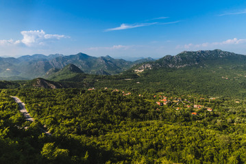 Naklejka na ściany i meble Montenegro landscape with balkan mountain village, road and rocks by cloudy day. Montenegrin wild nature scenery panoramic view with small town in the mountains valley. Freedom and adventure concept.
