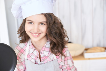 Beautiful girl. Little cook. White cap. Brown curly hair