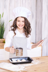 Light wooden background. Cooking buns. Girl with tablet in kitchen