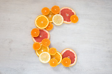 Vitamin c symbol made of sliced orange, grapefruit, mandarin and lemon on the bright wooden background