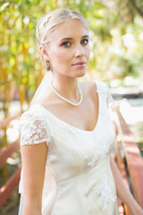 Pretty blonde bride in pearl necklace standing on a bridge