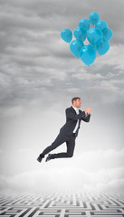 Businessman flying with balloon against cloudy sky over maze