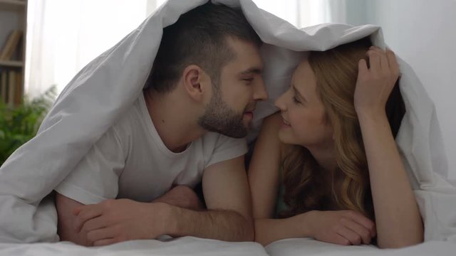 Tender couple kissing under blanket, happy newlyweds enjoying honeymoon, love
