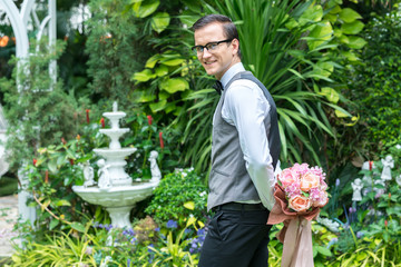 Groom holds a bouquet to the bride in the garden.