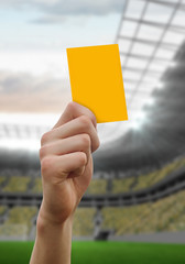 Hand holding up yellow card against football stadium