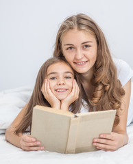 Young mother and daughter reading a book on the bed