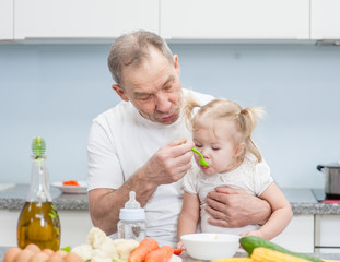 Senior man feeding baby girl with a spoon at kitchen