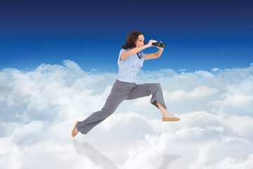 Cheerful classy businesswoman jumping while holding binoculars against bright blue sky over clouds