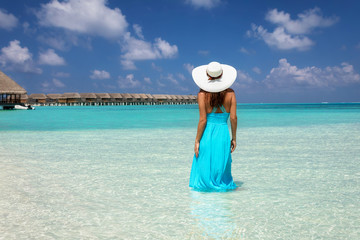 Fototapeta na wymiar Attraktive Frau in blauem Kleid steht in dem türkisen Meer der tropischen Malediven