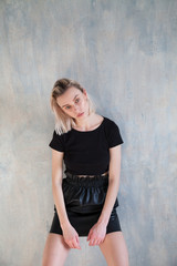 Naklejka premium trendy blonde woman in black dress posing the old wall