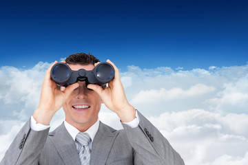 Businessman holding binoculars against bright blue sky over clouds