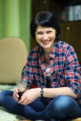 Obraz premium A beautiful smiling woman with a glass in her hand crosses her legs.